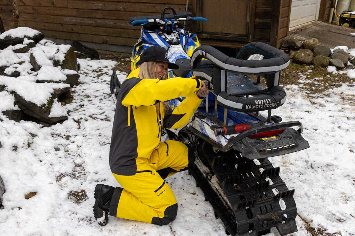 Blonde woman wearing yellow jacket installs dog carrier on Ski-Doo snowmobile