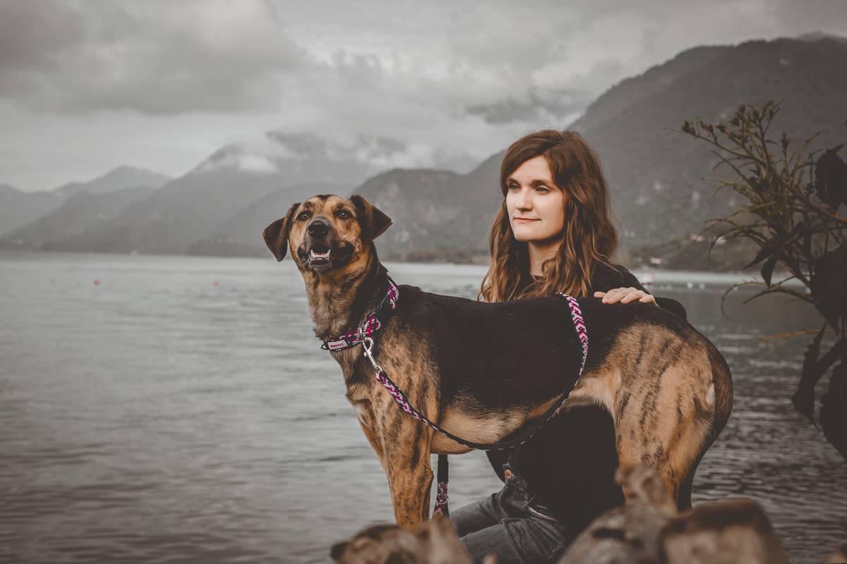 Woman sits happily on a rock beside her dog with a pink leash and collar