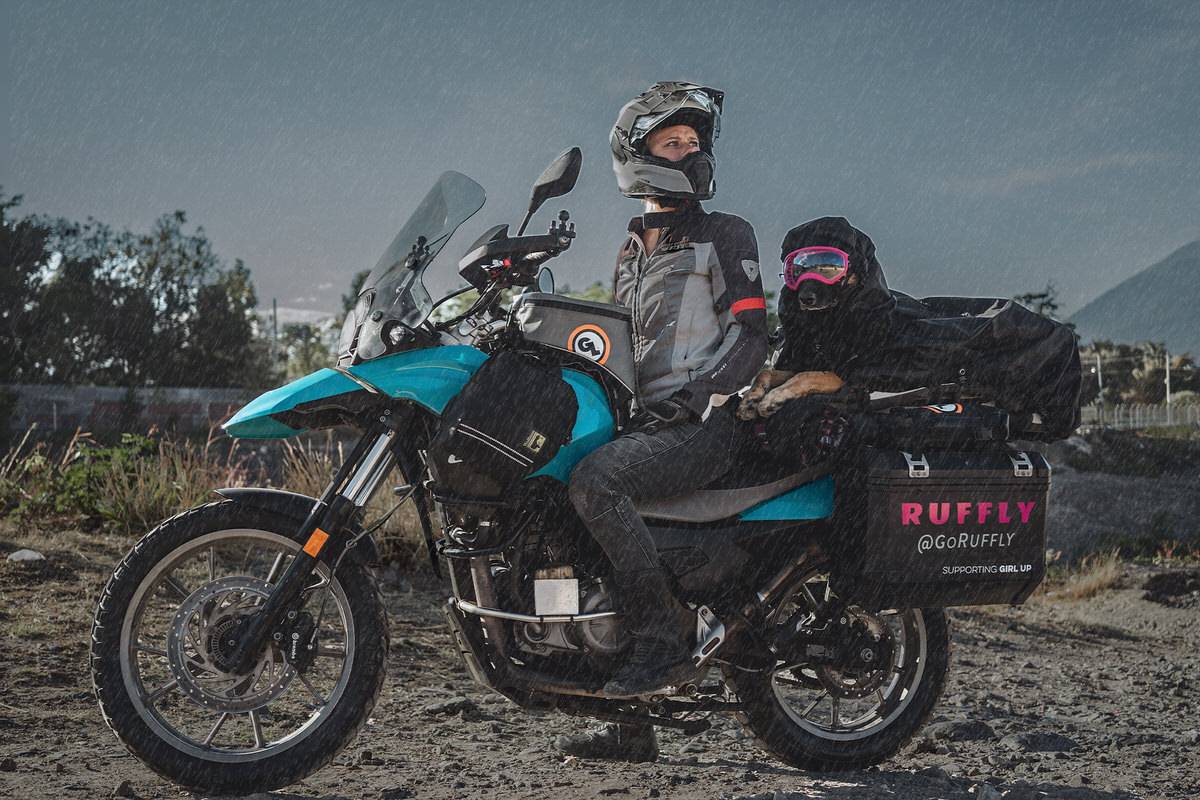 Woman stops on a motorcycle dog carrier in the rain with a dog under a rainfly