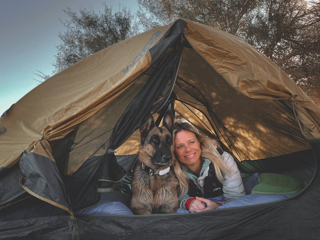 Woman and German shepherd dog lay together in a camping tent and look out