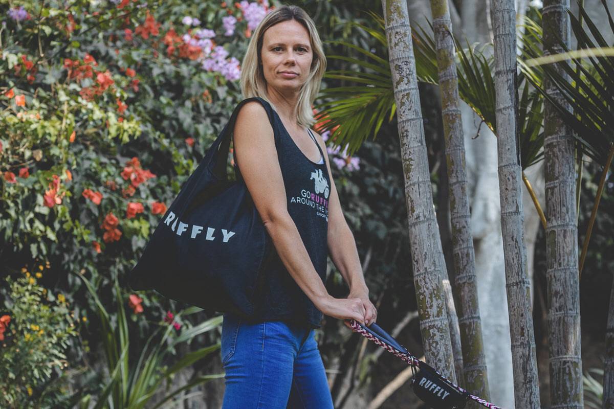 Blond woman holds a dog leash with a black RUFFLY tote bag on her shoulder