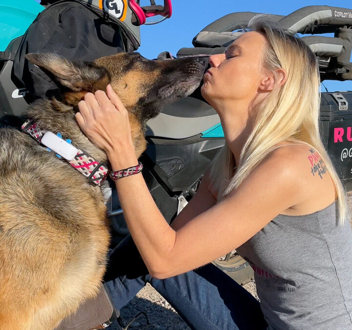 Woman and German Shepherd kiss in front of turquoise motorcycle